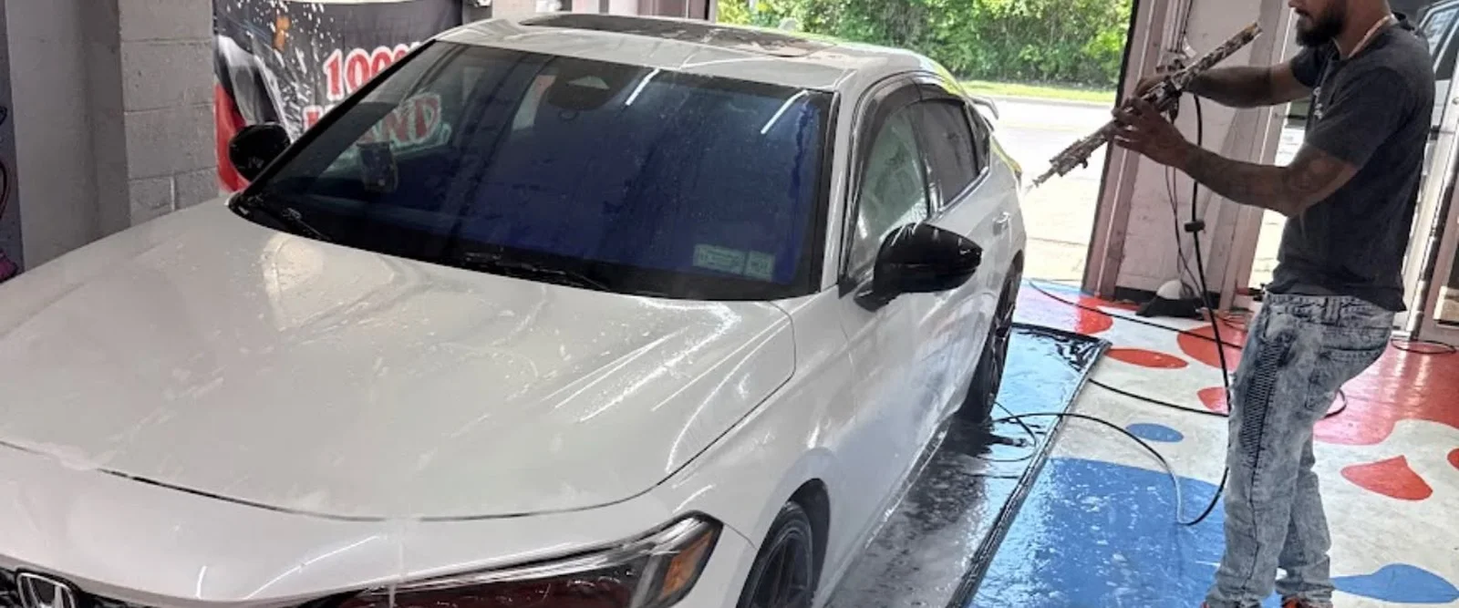 Technician foam washing a white Honda Civic inside the Guinea Pig Auto Detailing shop in Islip Terrace