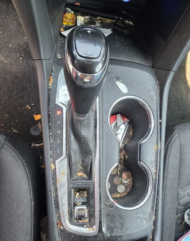 Dirty car center console with crumbs, coins and sticky residue in the cupholders before an interior detail