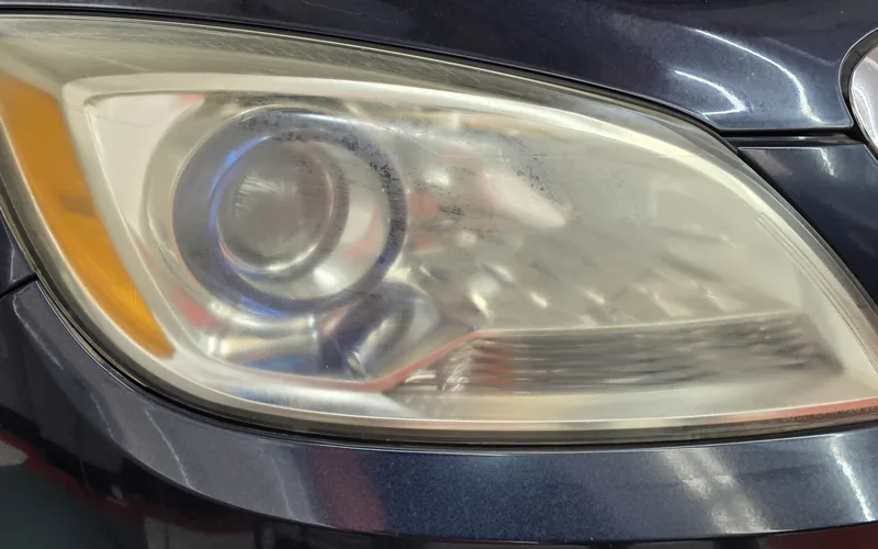 Cloudy, yellowed headlight on a dark blue Buick before headlight restoration