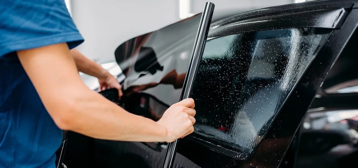 Installer fitting a strip of tint film to a side window